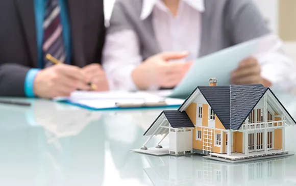 Home replica with property selling experts discussing real estate documents in the background.