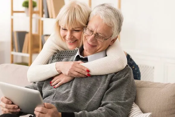 Elderly couple enjoying happy moments together at home while watching content on a tablet.
