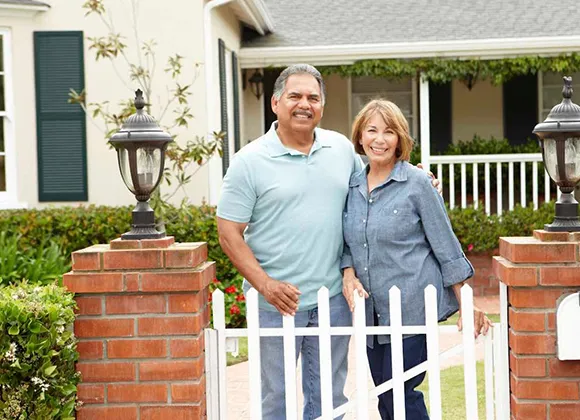Happy elderly couple standing together by the home fence, enjoying their downsized property.
